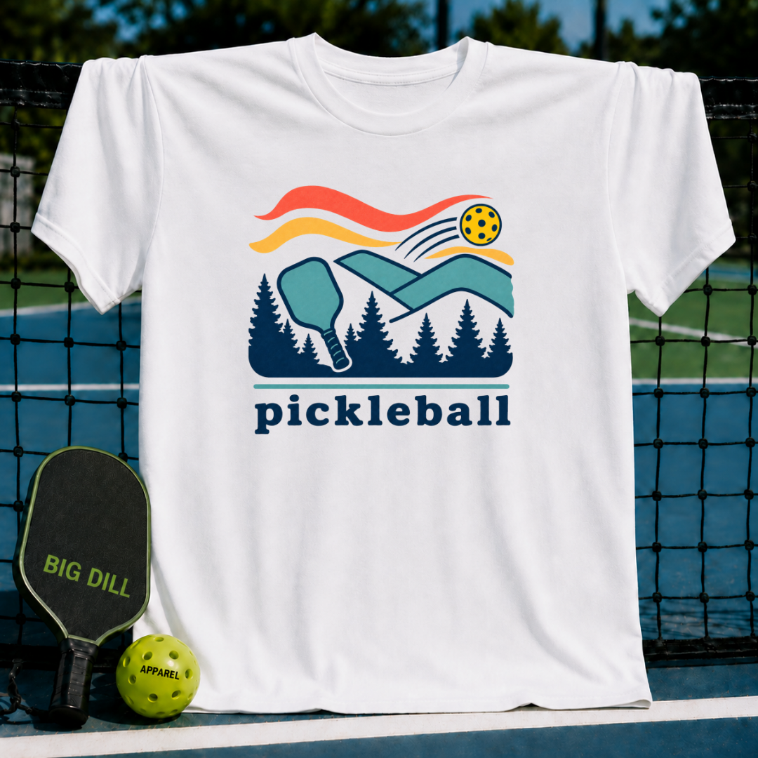 White crew neck t-shirt featuring a colorful pickleball court, paddle, and forest graphic with the word pickleball below.