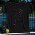 Black cotton t-shirt featuring a white pickleball paddle constellation design against a starry night sky graphic.