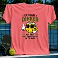 Coral pink crewneck t-shirt featuring a cartoon pickleball character with sunglasses and the text Official Dinker.