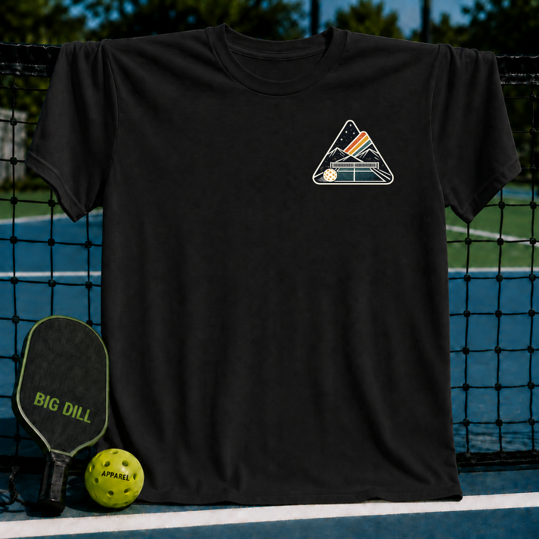 Black unisex t-shirt featuring a mountain and pickleball court crest graphic, displayed on a pickleball net background.