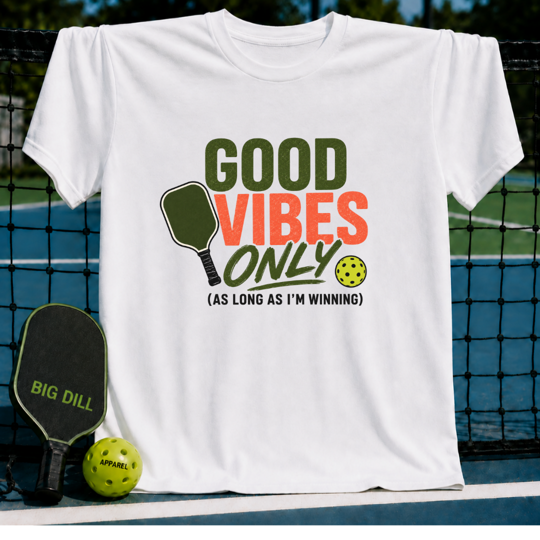White unisex t-shirt featuring olive, rust, and cream text with a pickleball paddle and ball graphic on a court background.