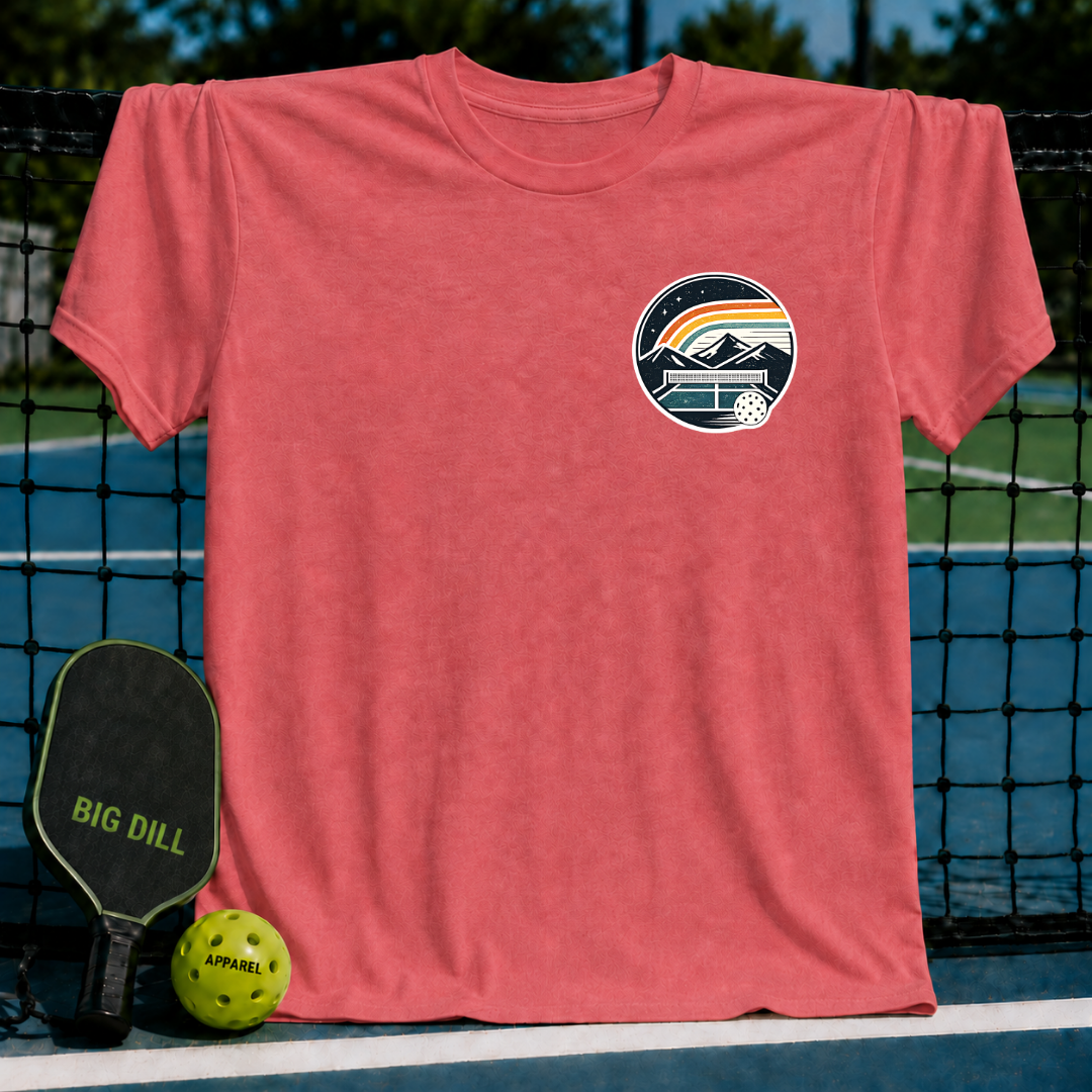 Coral unisex t-shirt featuring a circular pickleball court crest graphic with mountains and a rainbow on a pickleball court.