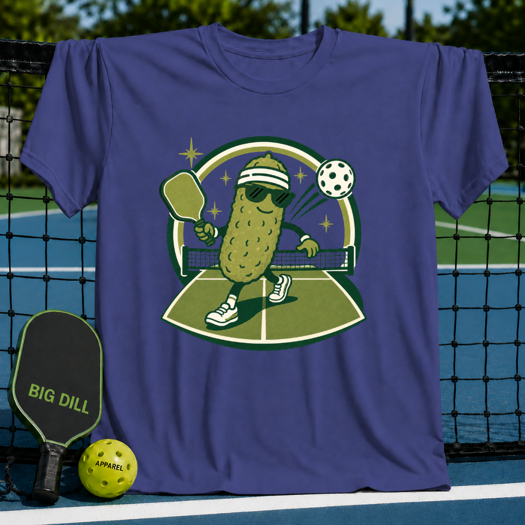 Purple crewneck t-shirt featuring a cartoon pickle playing pickleball on a court with a paddle and ball.