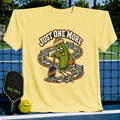 Light yellow crewneck t-shirt featuring a cartoon pickle playing pickleball with the text Just One More.