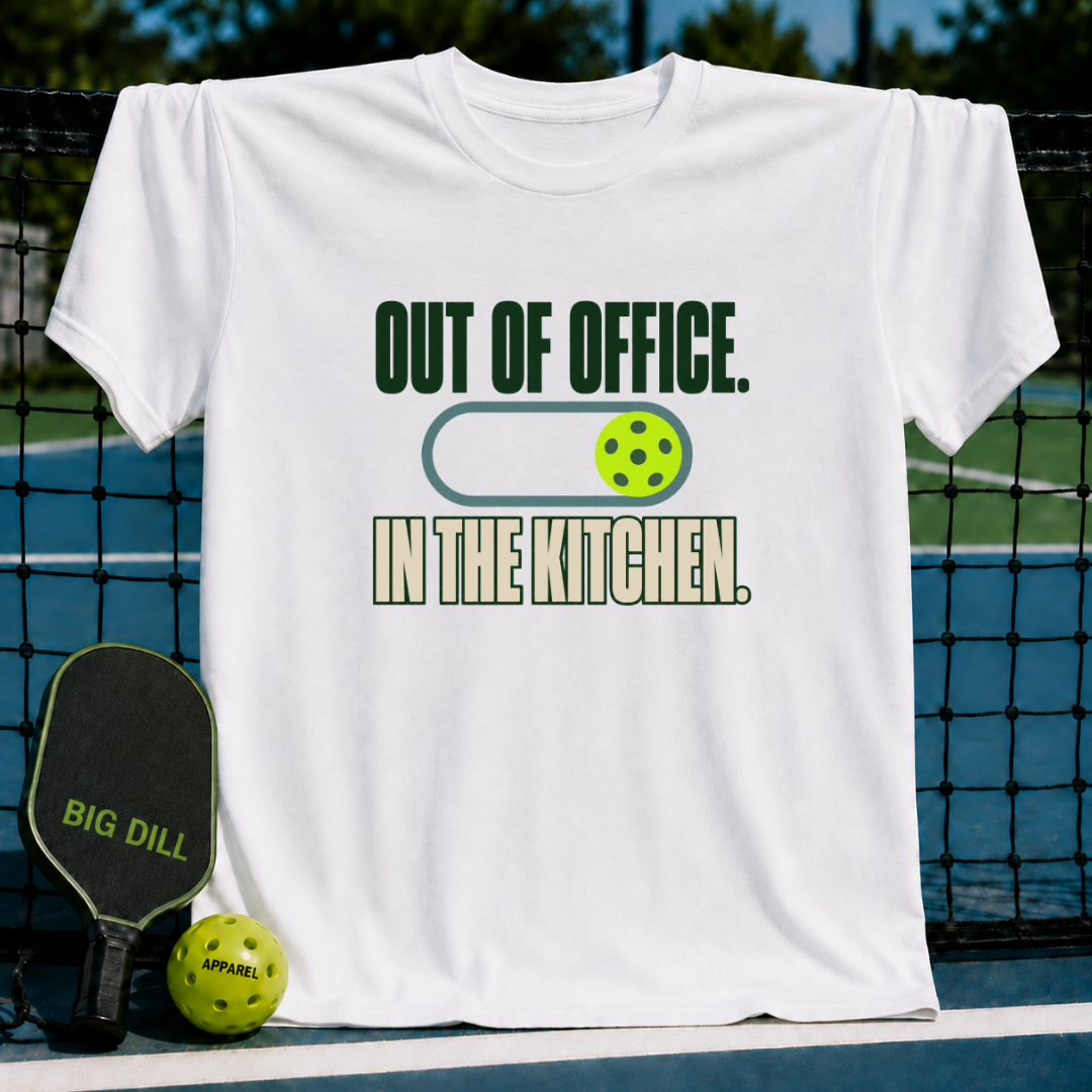 White crewneck t-shirt featuring a green Out of Office In the Kitchen pickleball graphic, displayed on a pickleball court.