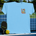 Light blue unisex t-shirt featuring a retro mid-century pickleball graphic on a pickleball court background.
