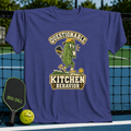 Purple crewneck t-shirt featuring a cartoon pickle playing pickleball with the text Questionable Kitchen Behavior.