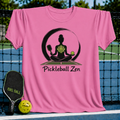 Pink t-shirt featuring a zen meditation graphic with a pickleball paddle and ball, displayed on a pickleball court net.