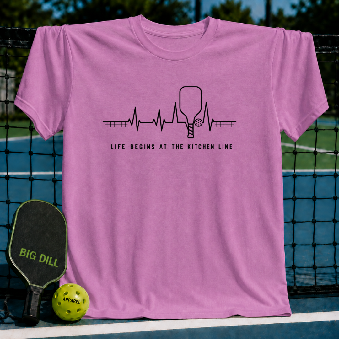 Orchid pink unisex t-shirt featuring a black heartbeat graphic with a pickleball paddle and the text Life Begins At The Kitchen Line.