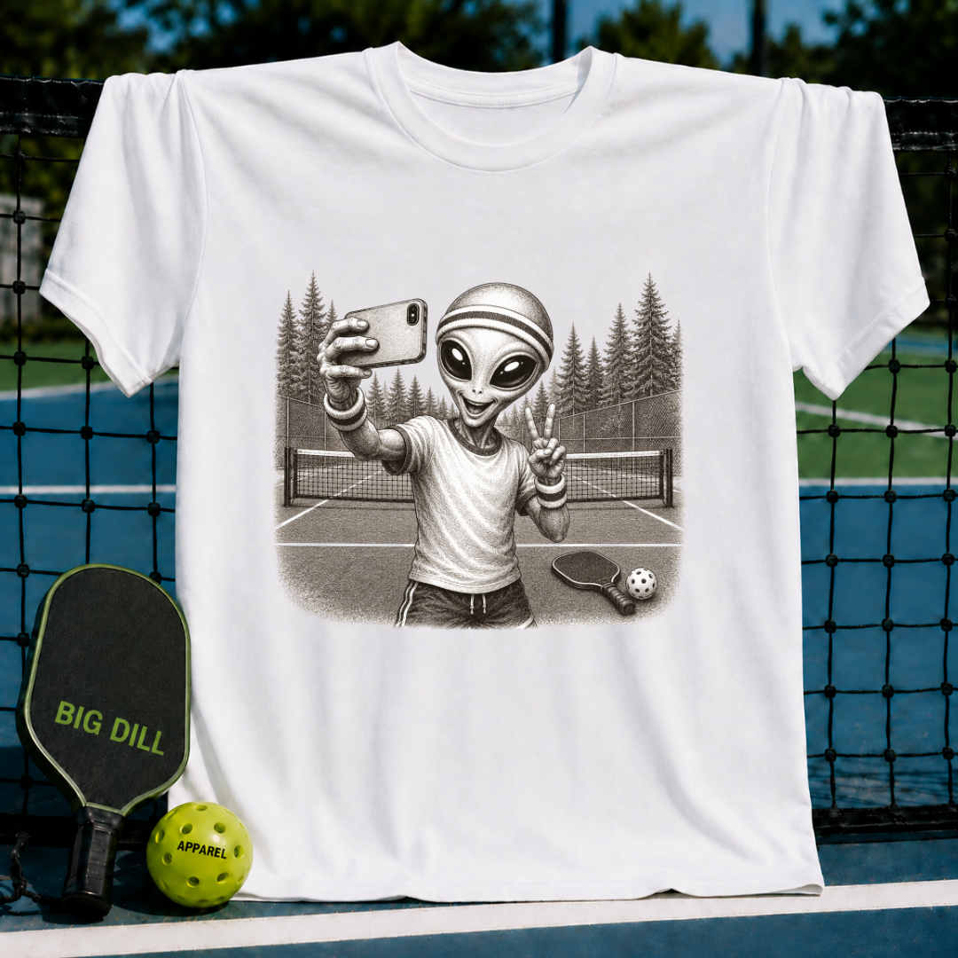 White t-shirt featuring a vintage-style illustration of an alien taking a selfie on a pickleball court.