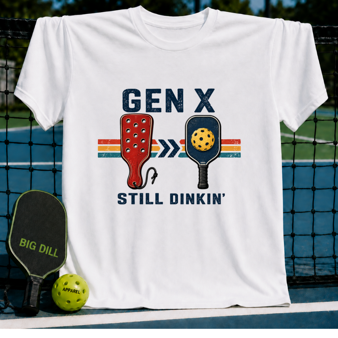 Cream unisex t-shirt featuring a retro Gen X Still Dinkin' pickleball graphic, displayed on a court net.