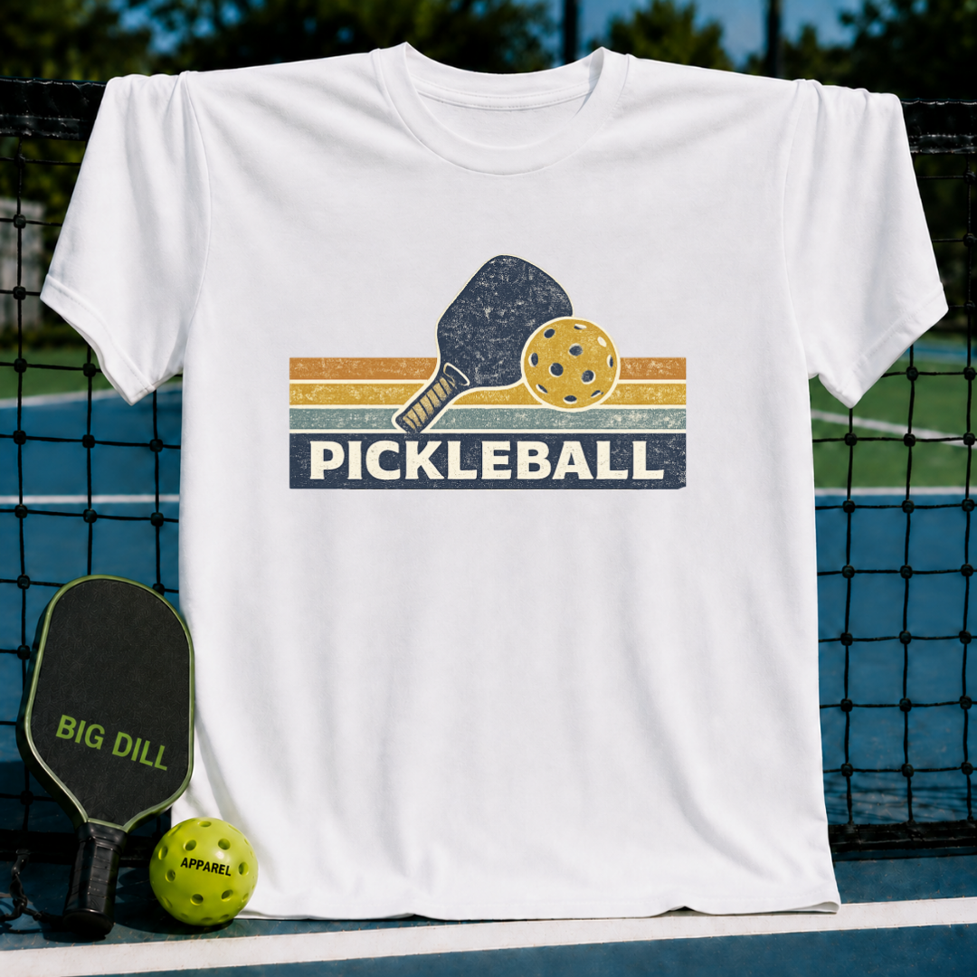 White vintage-style cotton t-shirt featuring a retro pickleball paddle and ball graphic with striped sunset colors.