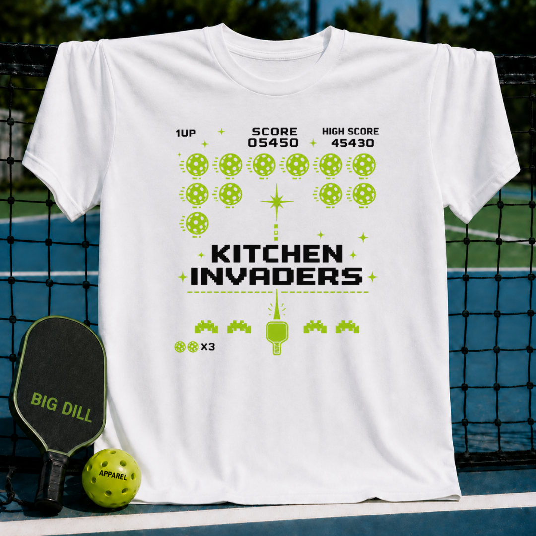White unisex t-shirt featuring a green pixel-art arcade game graphic with pickleballs, score counters, and paddle design.