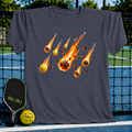 Charcoal grey unisex t-shirt featuring a vibrant graphic of flaming pickleballs falling like a meteor shower.