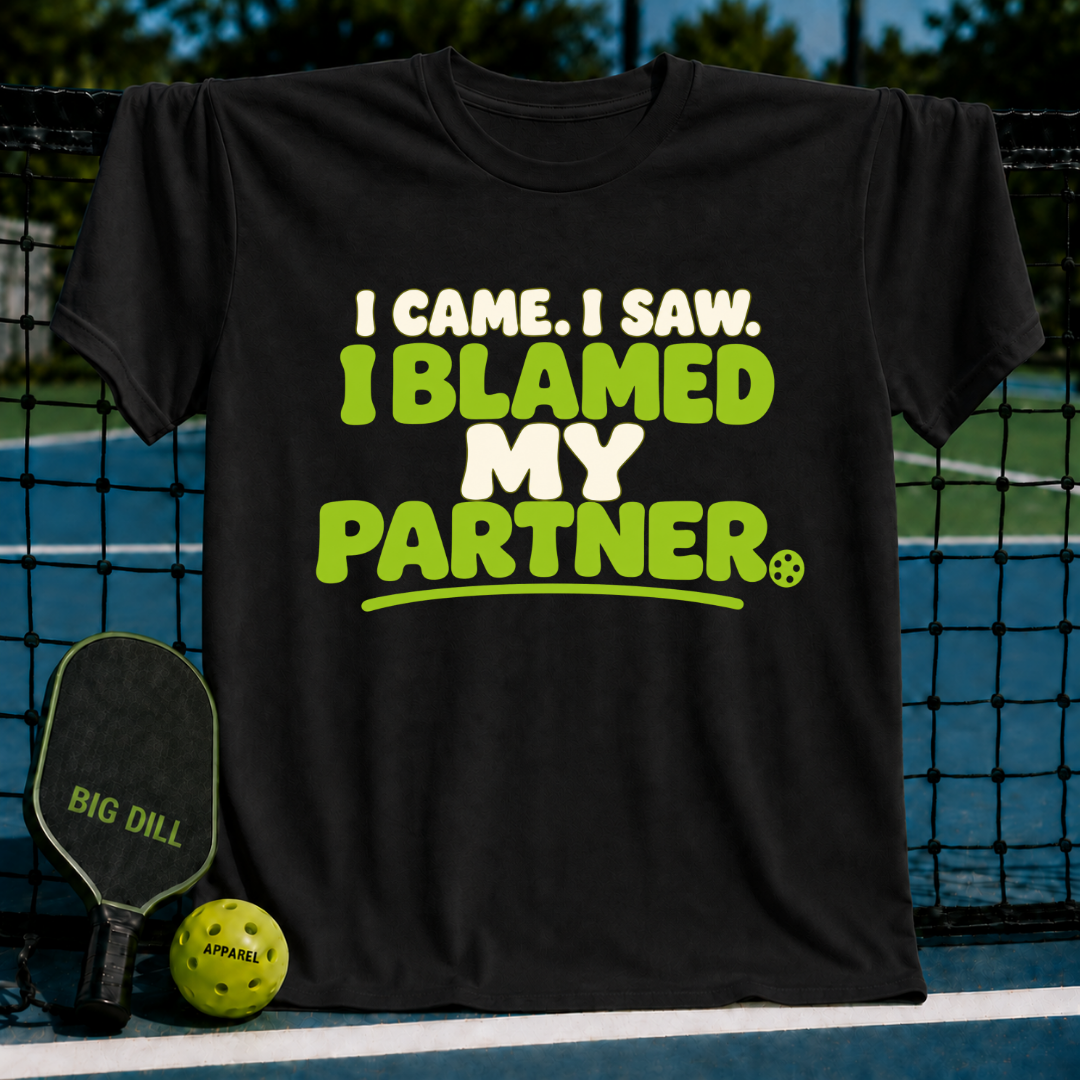 Black cotton T-shirt featuring green and white I Blamed My Partner pickleball text, displayed on a court with a paddle.