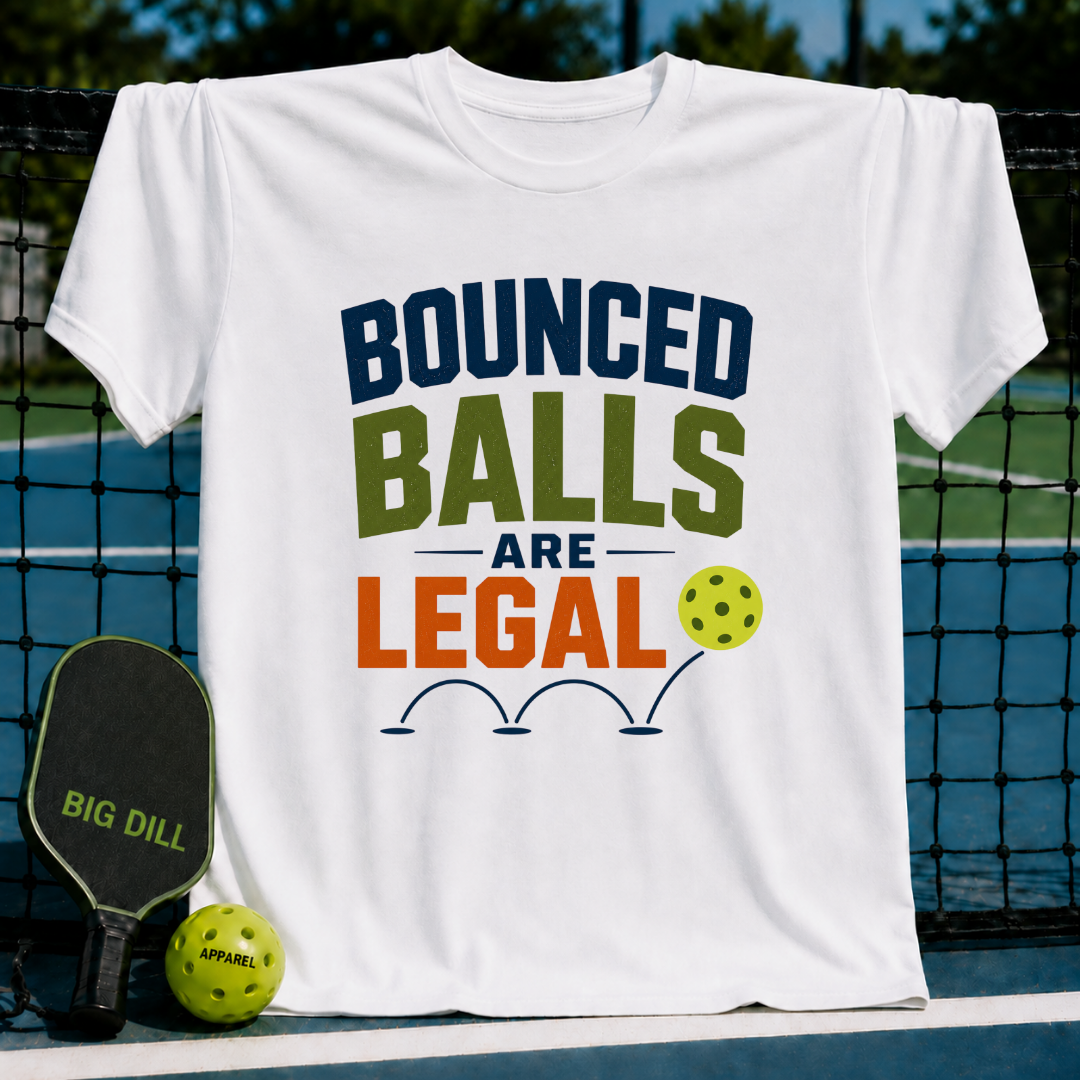 White unisex t-shirt featuring colorful Bounced Balls Are Legal pickleball typography, displayed on a court net.