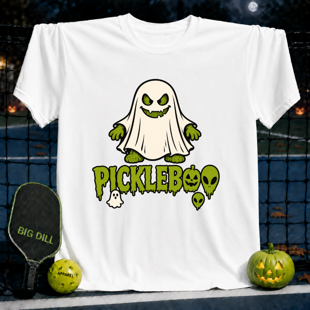 White unisex PickleBoo t-shirt featuring a green ghost pickle graphic, displayed on a pickleball court with a paddle and ball.