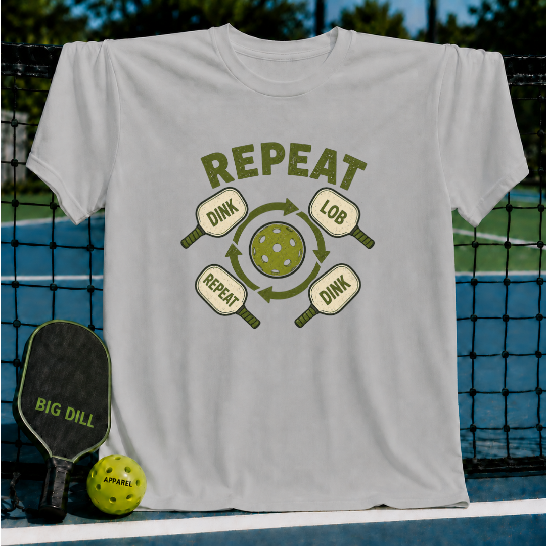 Light gray crew neck t-shirt featuring a green pickleball graphic with the text Dink, Lob, Dink, Repeat on a court background.