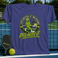 Purple crewneck t-shirt featuring a cartoon pickle playing pickleball with the text Dill With It on a court background.