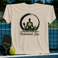 Beige crewneck t-shirt featuring a meditating figure with a pickleball paddle and ball, set against a pickleball court background.