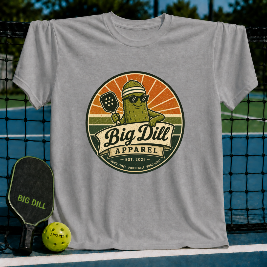 Grey unisex t-shirt featuring a retro pickleball mascot graphic with a sunset badge design on a pickleball court.