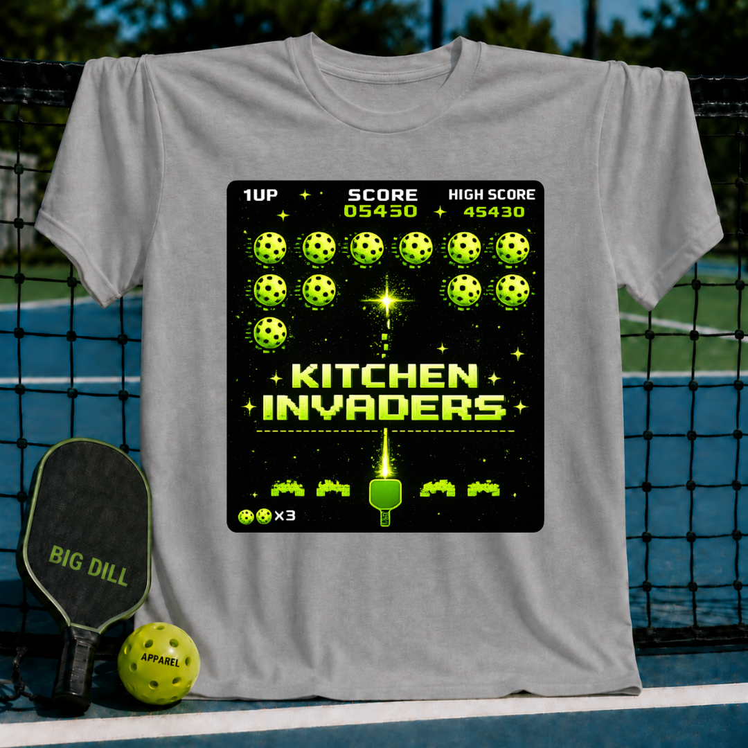 Grey unisex t-shirt featuring a retro pixel-art Kitchen Invaders graphic with pickleballs and a paddle on a pickleball court.