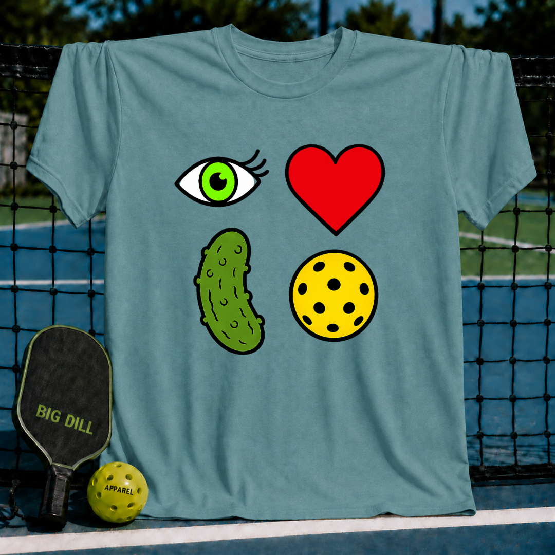 Blue-grey unisex t-shirt featuring a 2x2 grid of eye, heart, pickle, and ball icons, displayed on a pickleball court.