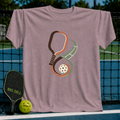 Mauve crewneck t-shirt featuring an infinity-shaped pickleball paddle and court graphic with a ball on a court background.