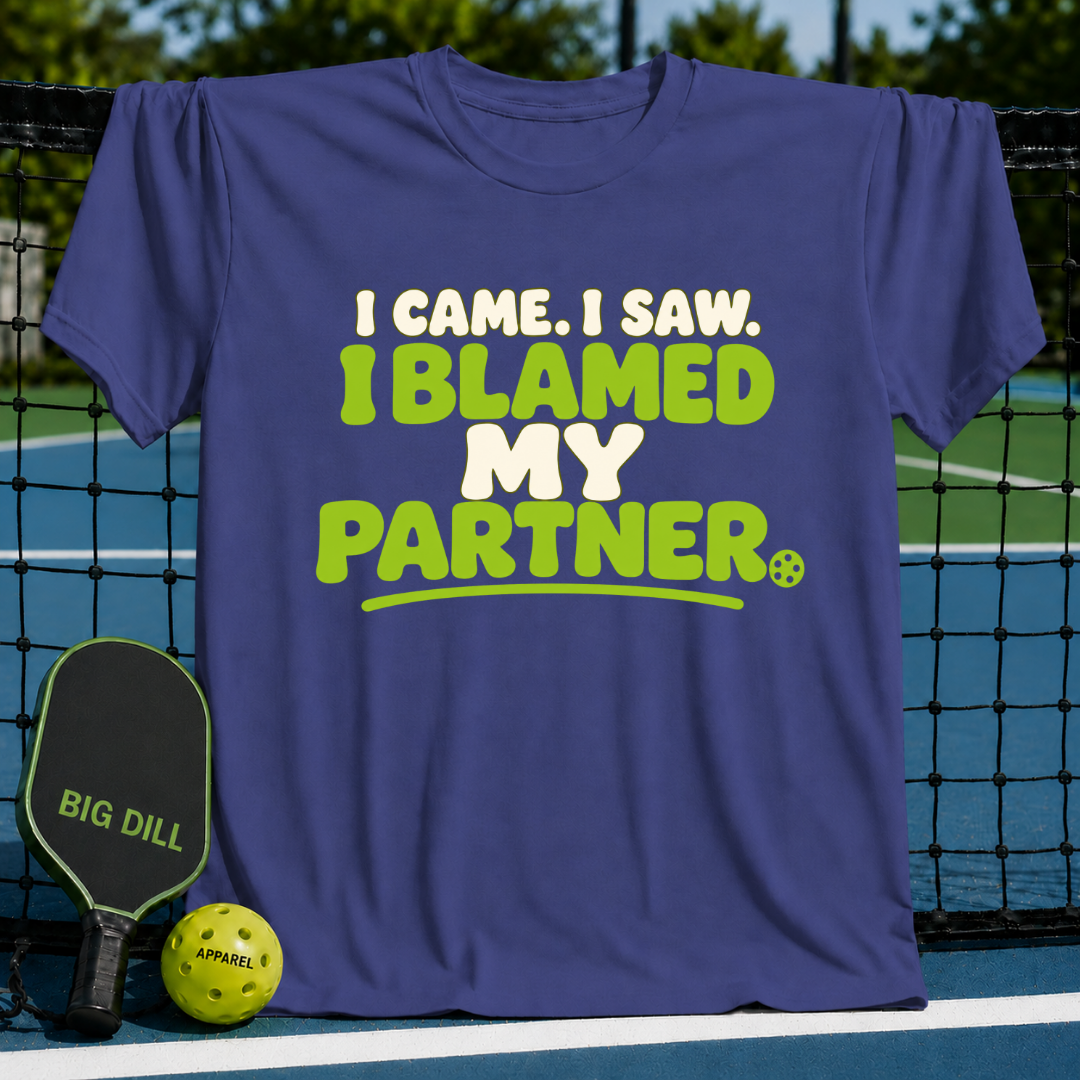Purple crewneck t-shirt with I Came, I Saw, I Blamed My Partner text in lime green and white on a pickleball court.