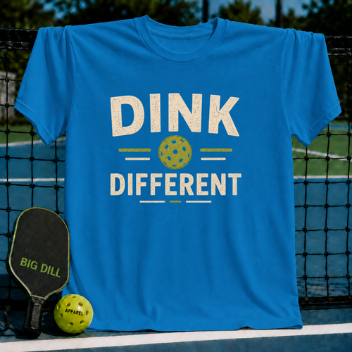 Bright blue Dink Different pickleball t-shirt with a distressed graphic, displayed on a court net with a paddle and ball.