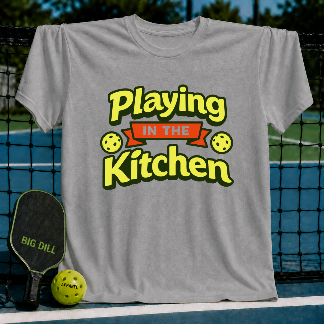 Grey crewneck t-shirt featuring a yellow and red Playing in the Kitchen pickleball graphic, displayed on a court background.