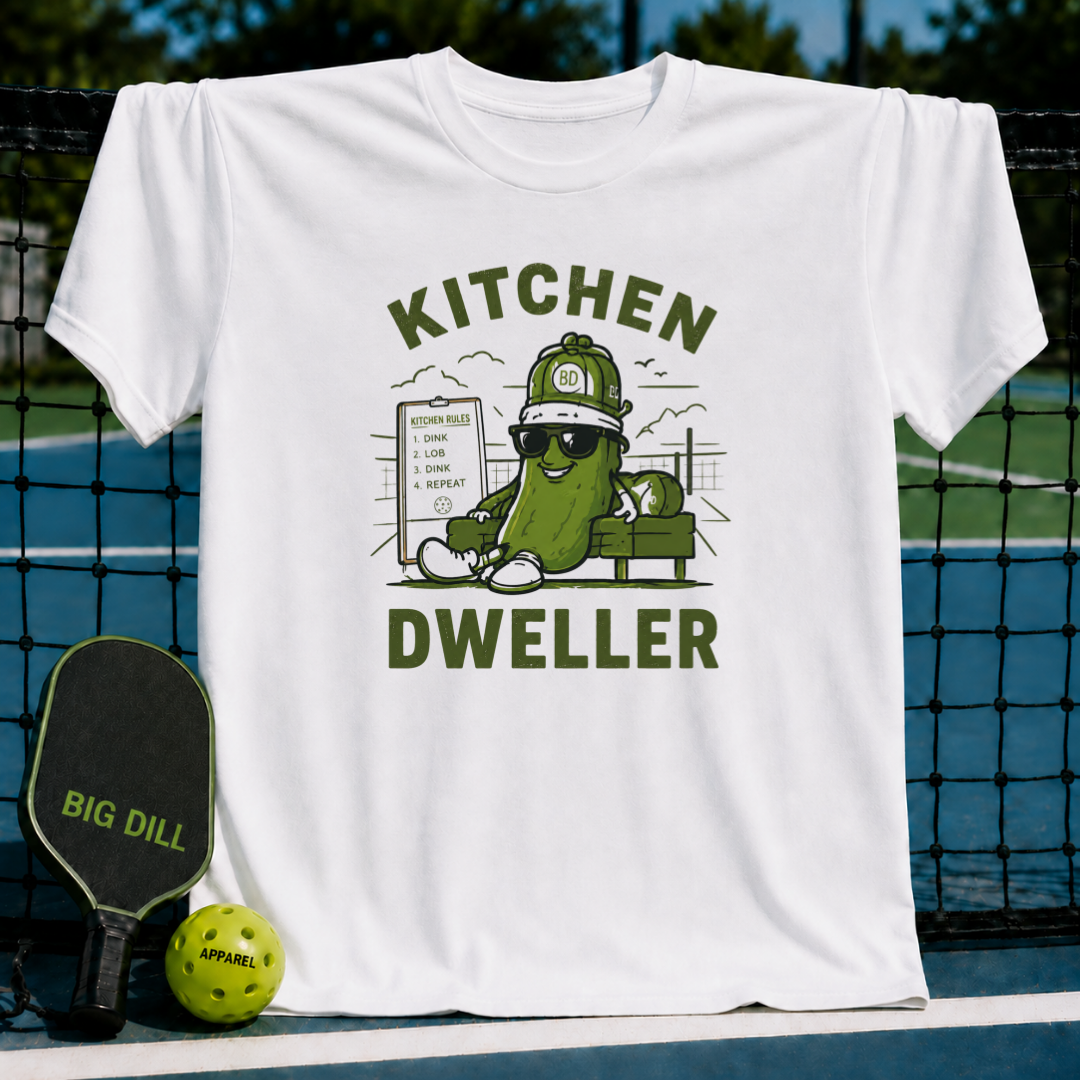 White crew neck T-shirt featuring a cartoon pickle wearing sunglasses and a hat with Kitchen Dweller pickleball graphic.