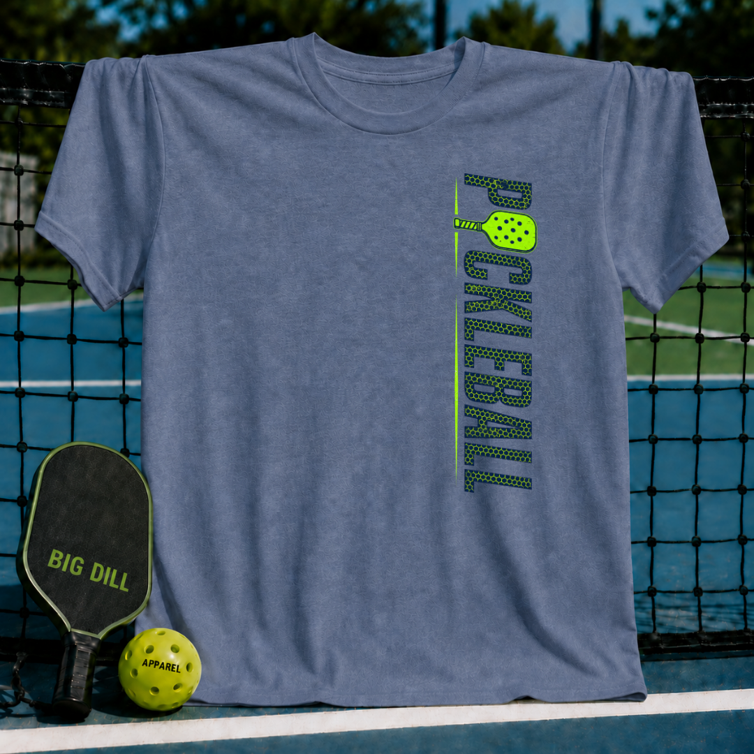 Muted mauve unisex t-shirt with vertical green Pickleball text and paddle graphic, displayed on a pickleball court net.
