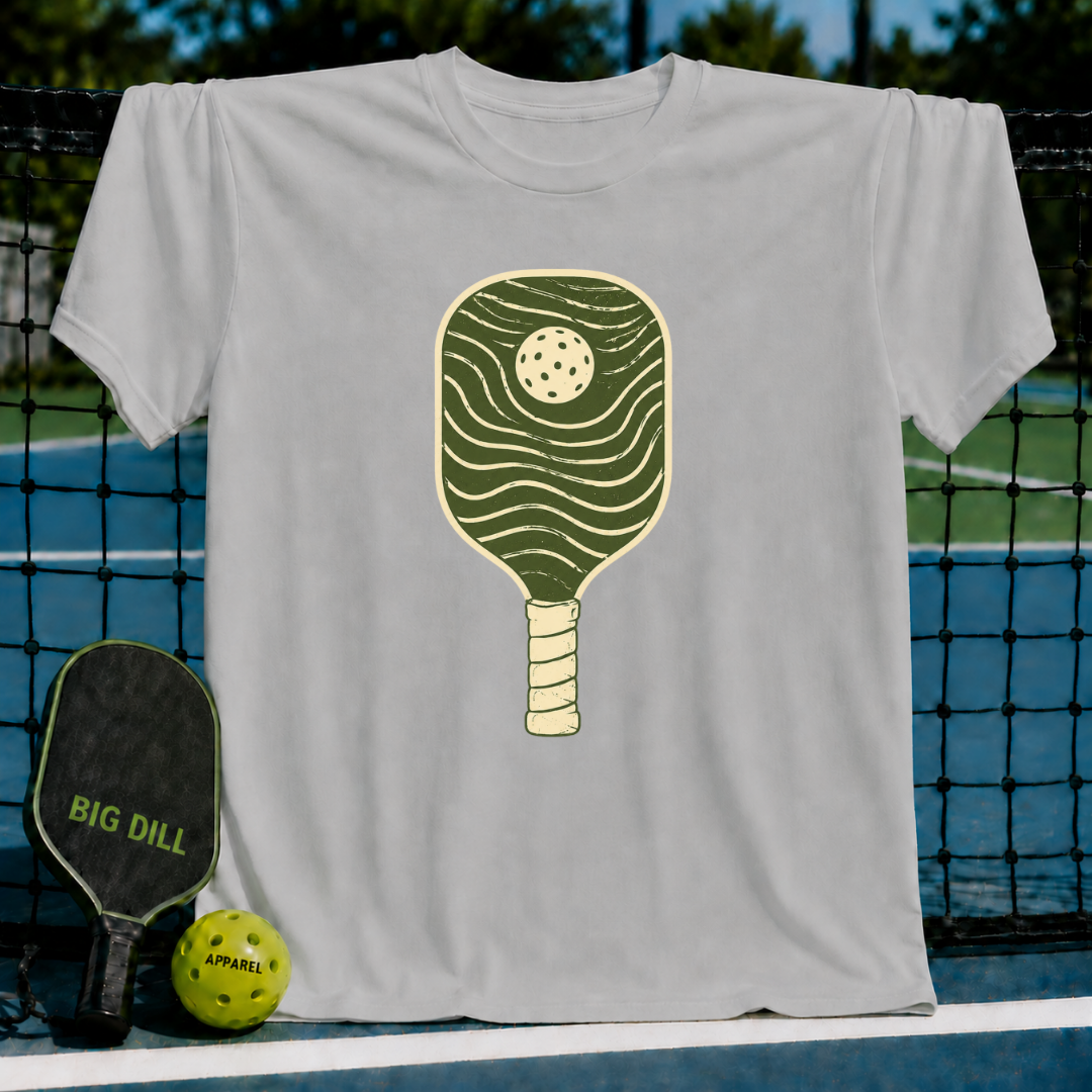 Cream unisex t-shirt featuring a minimalist forest green hand-drawn pickleball paddle with flowing wave lines.