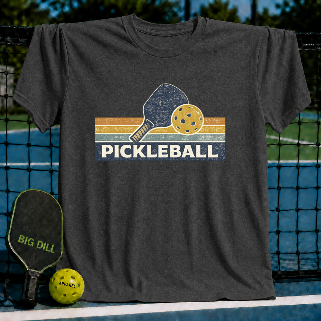 Charcoal grey vintage-style t-shirt featuring a retro pickleball paddle and ball graphic with striped sunset colors.