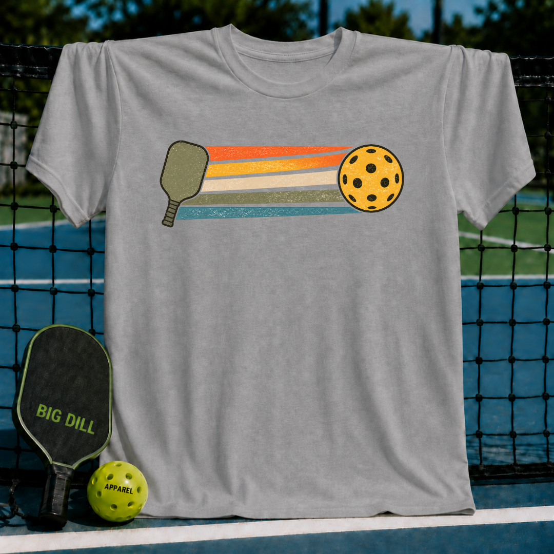 Grey unisex t-shirt featuring a retro pickleball paddle and ball graphic with colorful motion stripes on a court background.