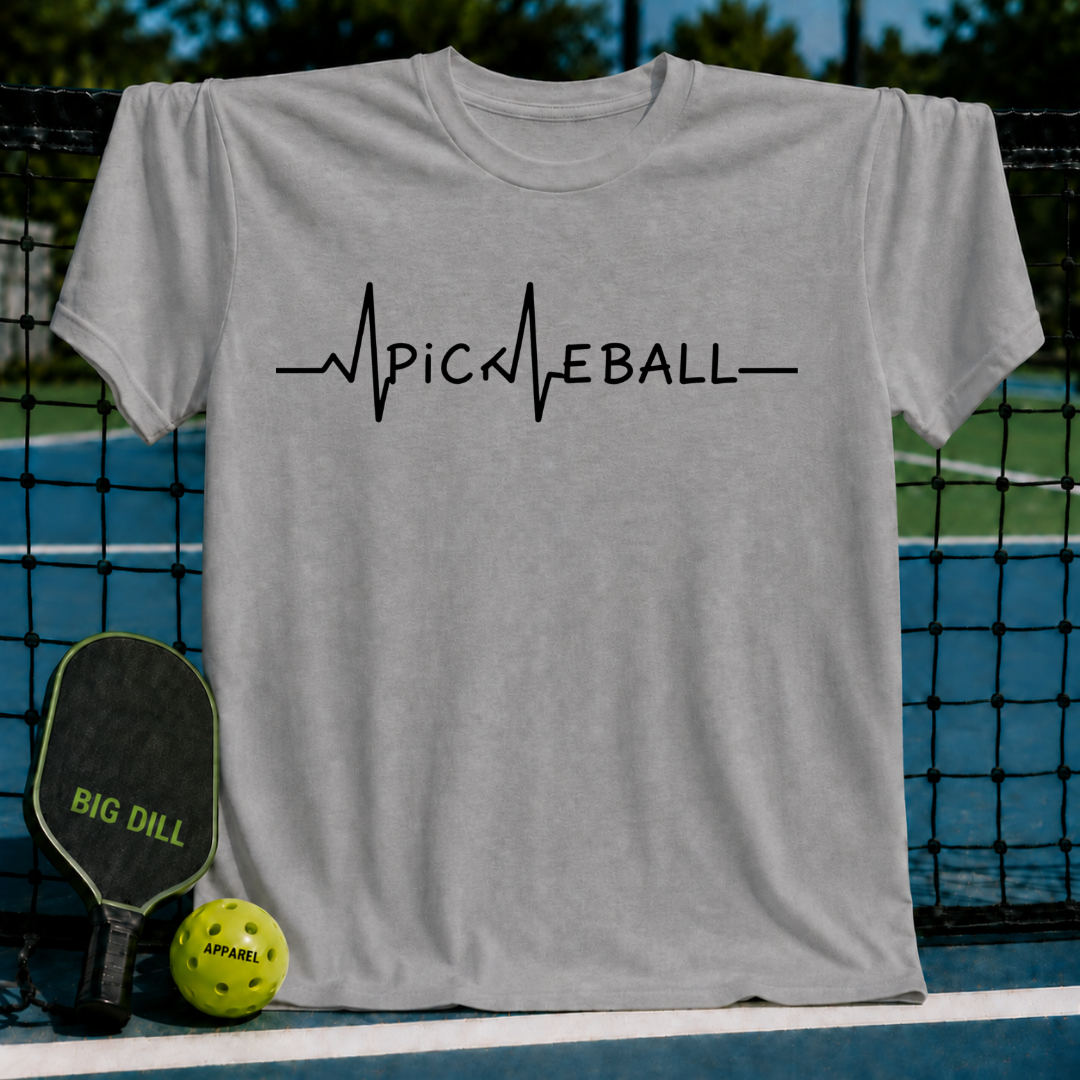 Light gray unisex t-shirt featuring a black EKG heartbeat line graphic that spells out PICKLEBALL on a pickleball court.