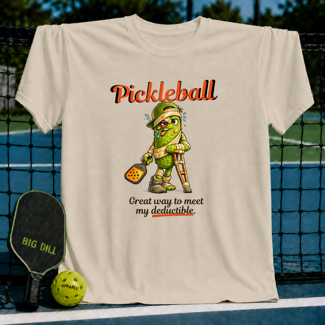 Beige unisex t-shirt featuring a cartoon pickle on crutches with a paddle and the text Pickleball: Great way to meet my deductible.