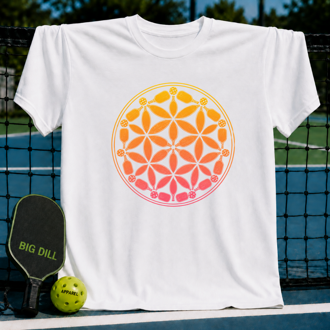 White t-shirt featuring an orange and yellow Flower of Life design made of pickleball paddles and balls on a court.