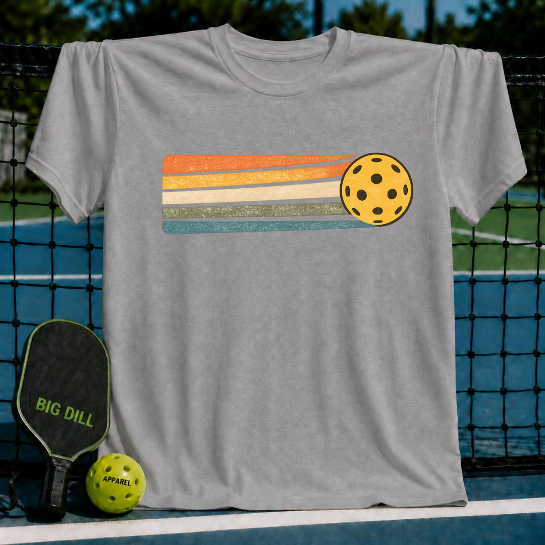 Grey unisex t-shirt featuring a yellow pickleball with retro orange, cream, and teal motion stripes on a pickleball court.