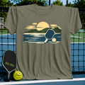Military olive unisex t-shirt featuring a painterly mountain and pickleball graphic in golden and navy tones.