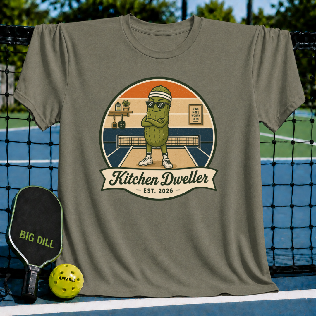 Olive green unisex t-shirt featuring a retro pickleball graphic with a pickle character and the text Kitchen Dweller.