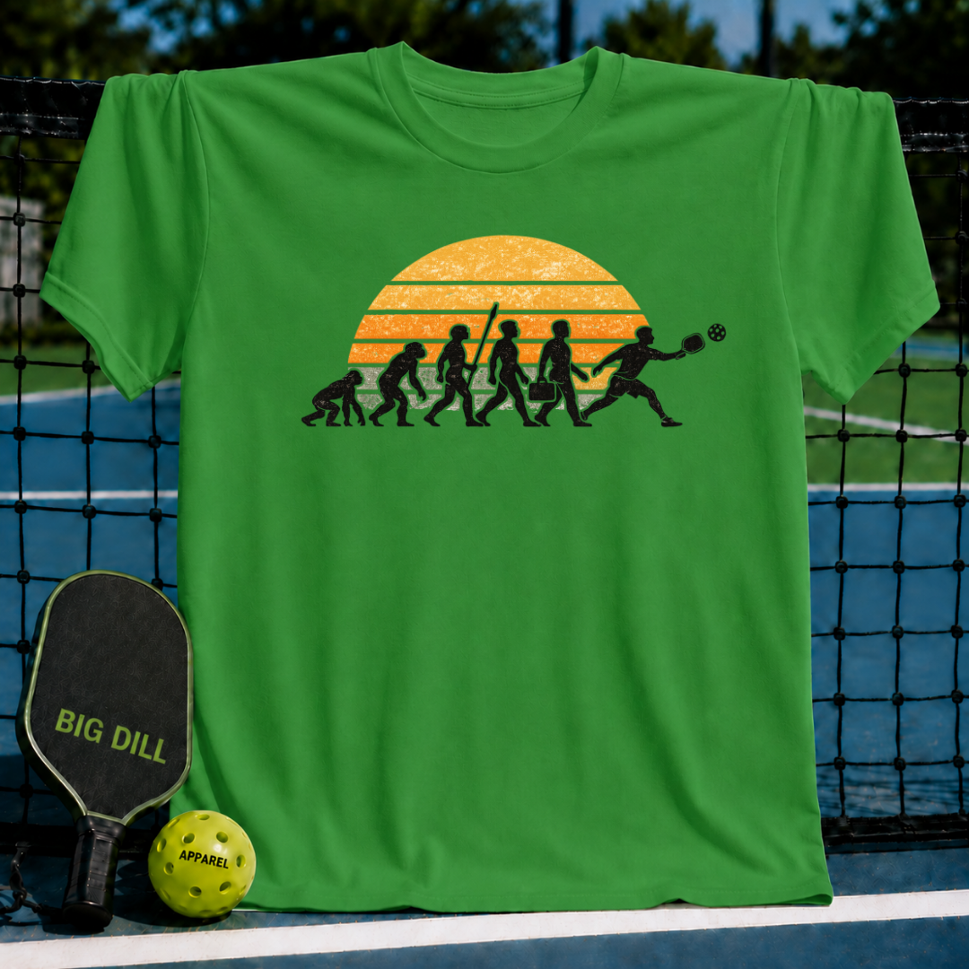 Green t-shirt featuring a retro sunset evolution graphic of a man playing pickleball, displayed on a court net.
