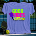 Periwinkle unisex t-shirt with neon green and pink pickleball graphic text on a tennis court background.