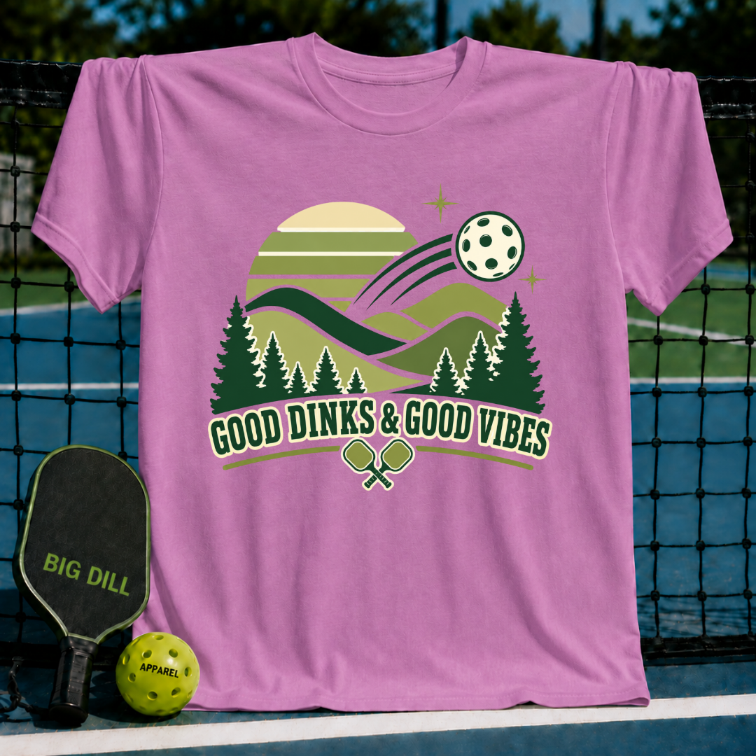 Pink cotton t-shirt featuring a pickleball-themed graphic with pine trees, a sun, and Good Dinks & Good Vibes text.