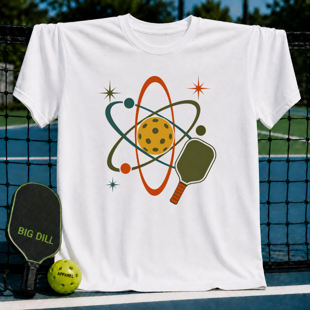 Cream unisex t-shirt featuring a retro mid-century atomic pickleball graphic in red and teal on a pickleball court.