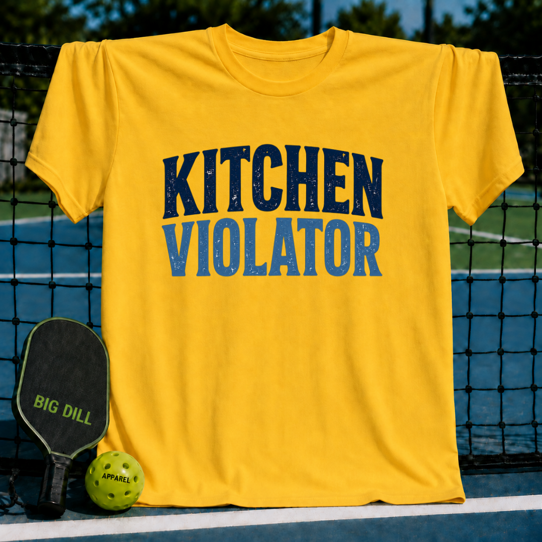 Bright yellow unisex t-shirt with distressed navy blue Kitchen Violator varsity lettering, displayed on a pickleball court.