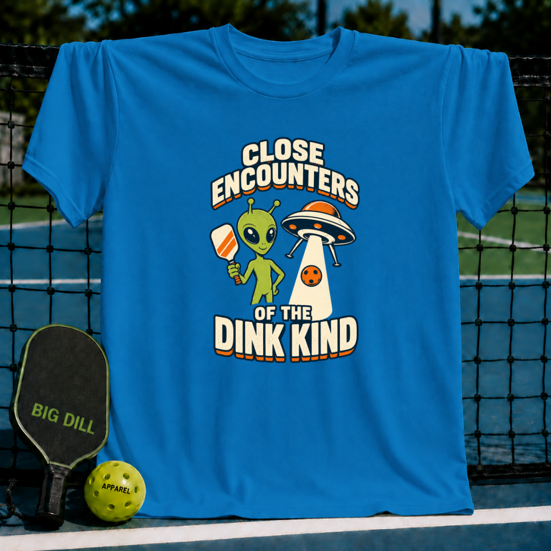 Bright blue crewneck T-shirt featuring a green alien holding a pickleball paddle next to a UFO graphic.