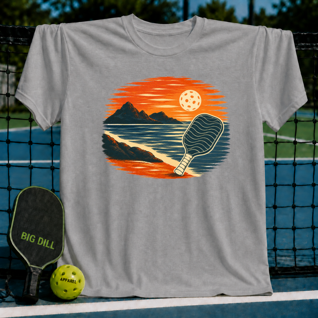 Grey unisex t-shirt featuring a vintage oval illustration of a pickleball paddle on a beach at sunset.
