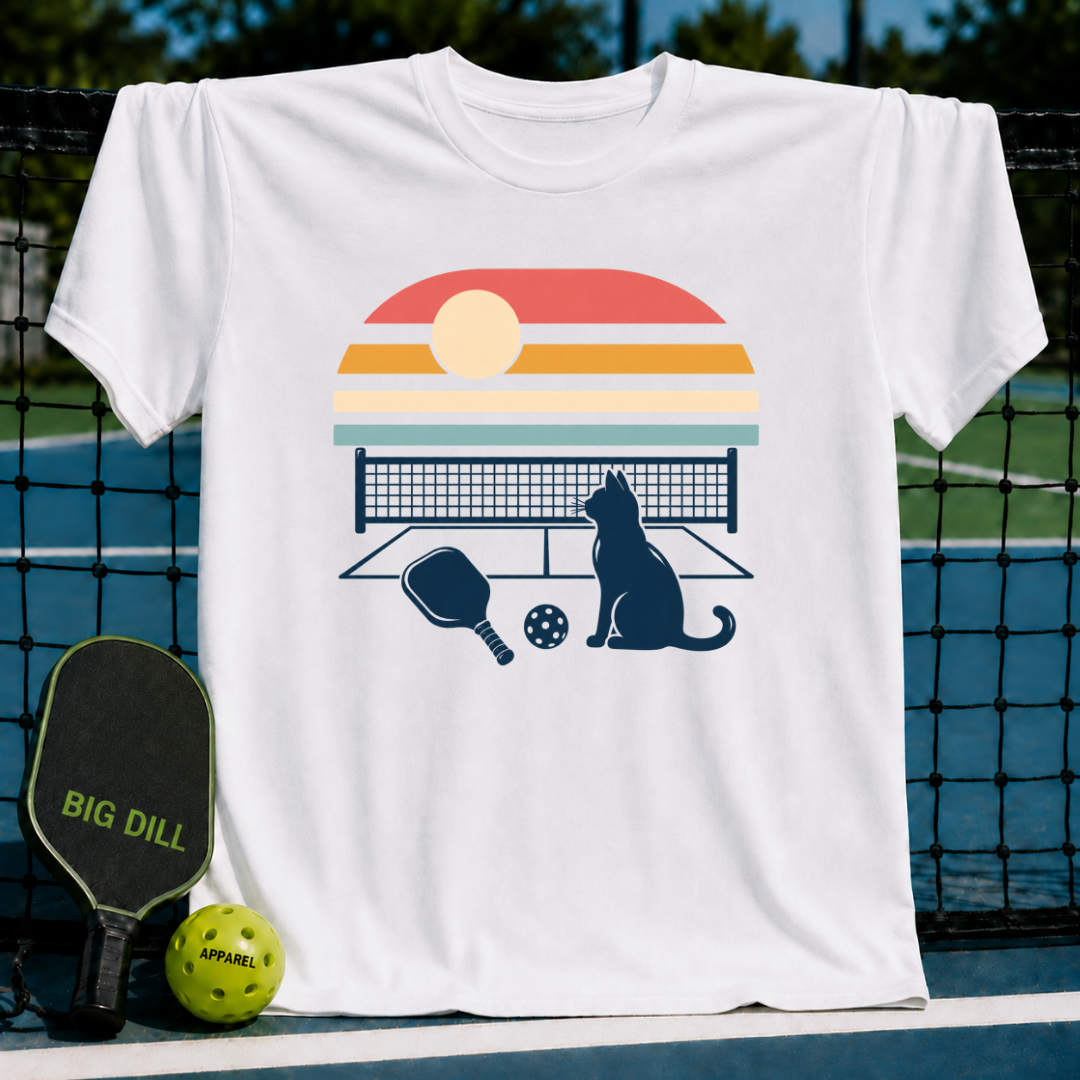 White cotton t-shirt featuring a retro sunset graphic with a cat, pickleball paddle, and ball on a court background.